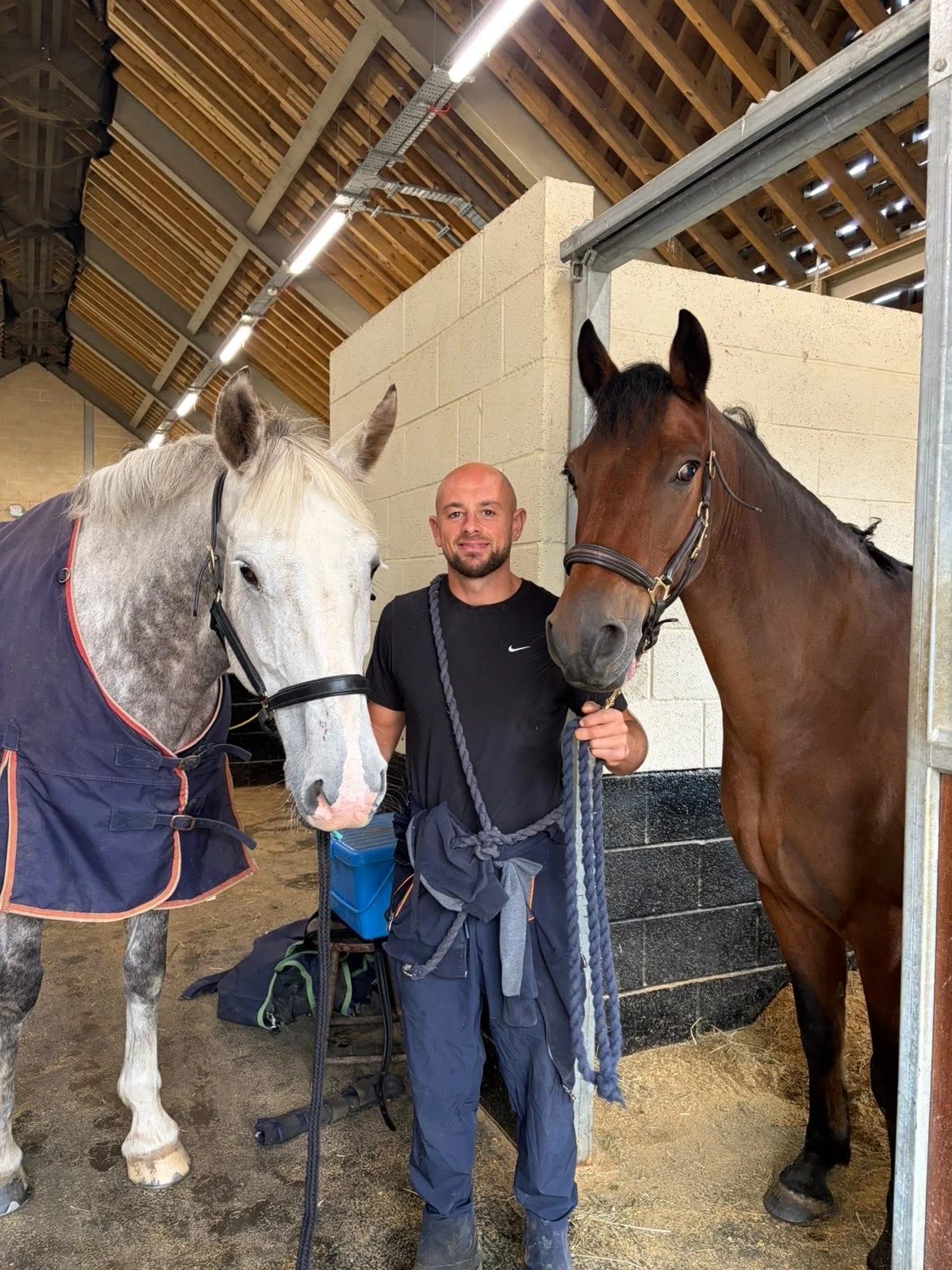 Paul in the stables with a grey horse and a bay horse